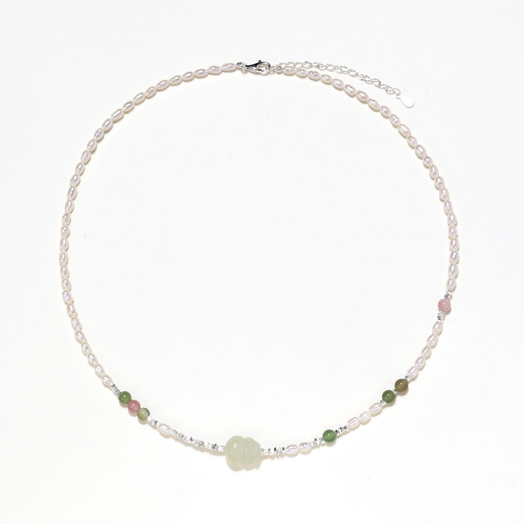 Delicate pearl necklace with pale green serpentine jade centerpiece and colorful agate beads on cream background