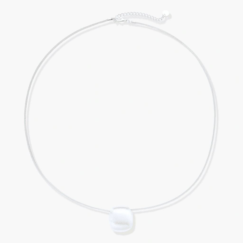 Minimalist brushed sterling silver dome pendant on delicate chain against cream background, showing matte textured finish