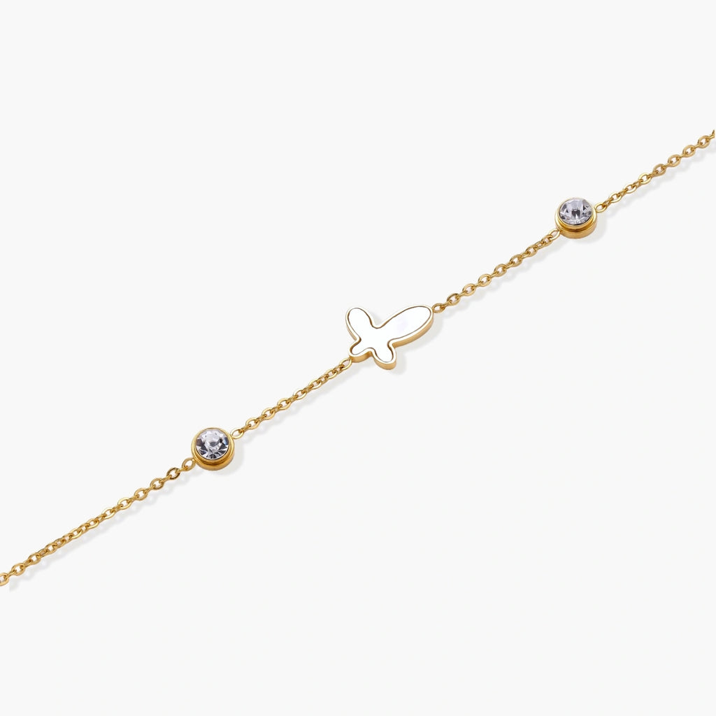 Gold chain bracelet with white mother of pearl butterfly pendant and two bezel-set crystals on cream background