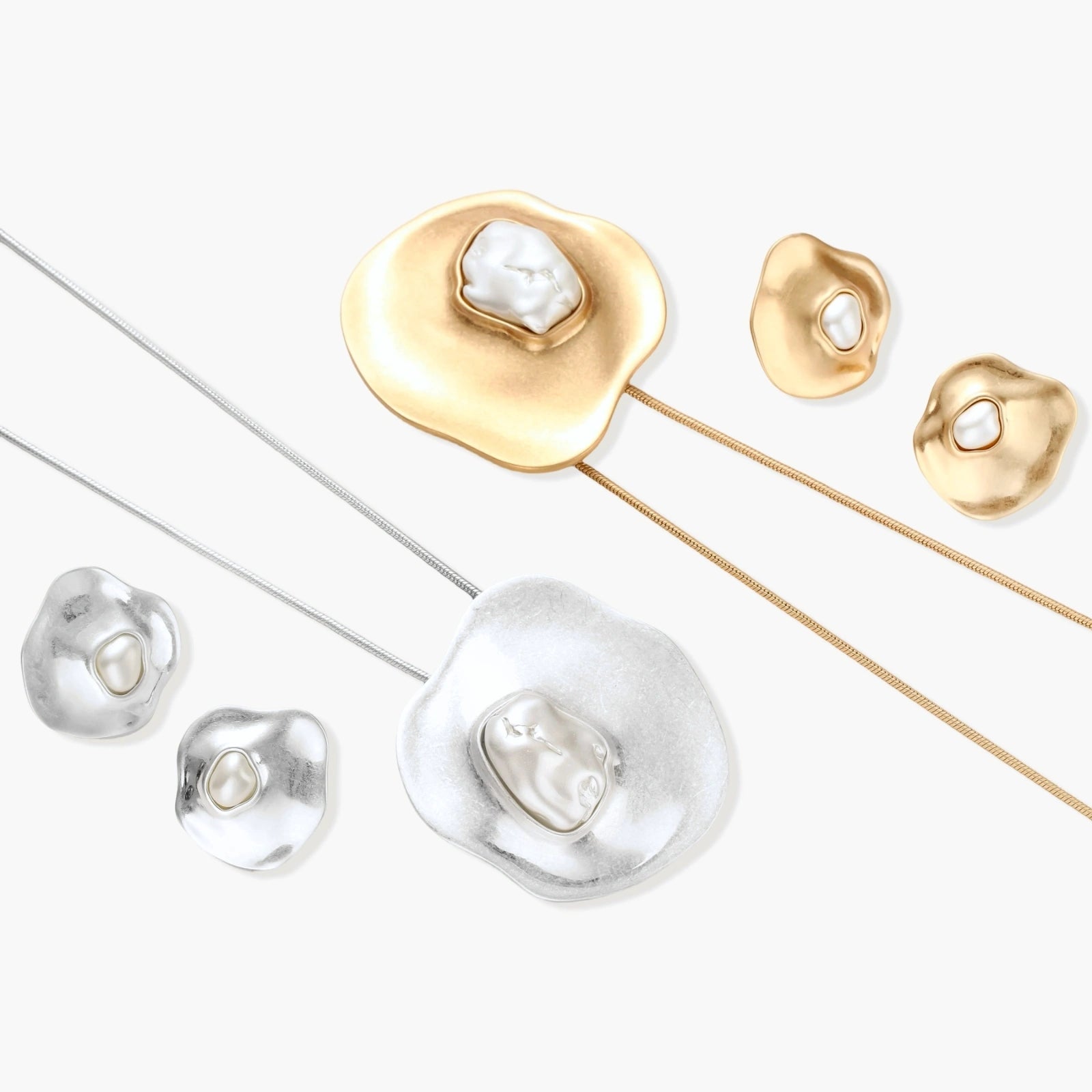 Close-up of organic gold-toned earrings and necklace with white baroque pearls on neutral background.