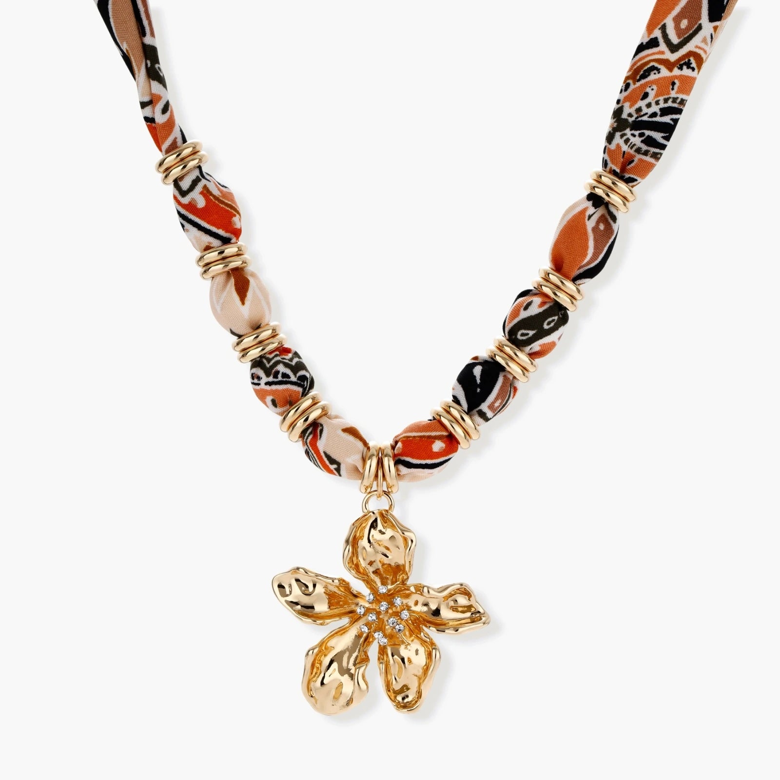 Vibrant patterned fabric necklace with gold-toned flower pendant featuring rhinestone center on white background