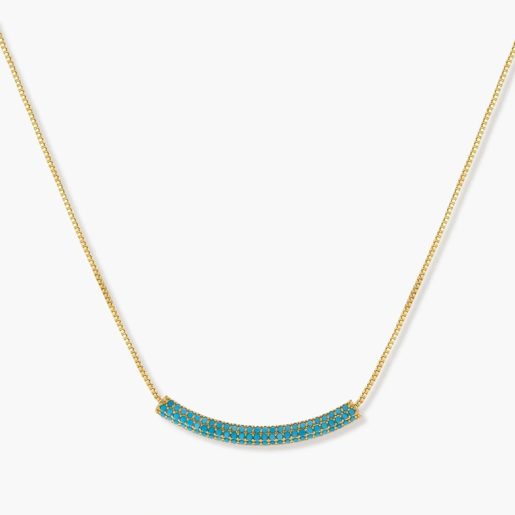 Gold-plated curved necklace and hoop earrings with turquoise cubic zirconia stones on white background.
